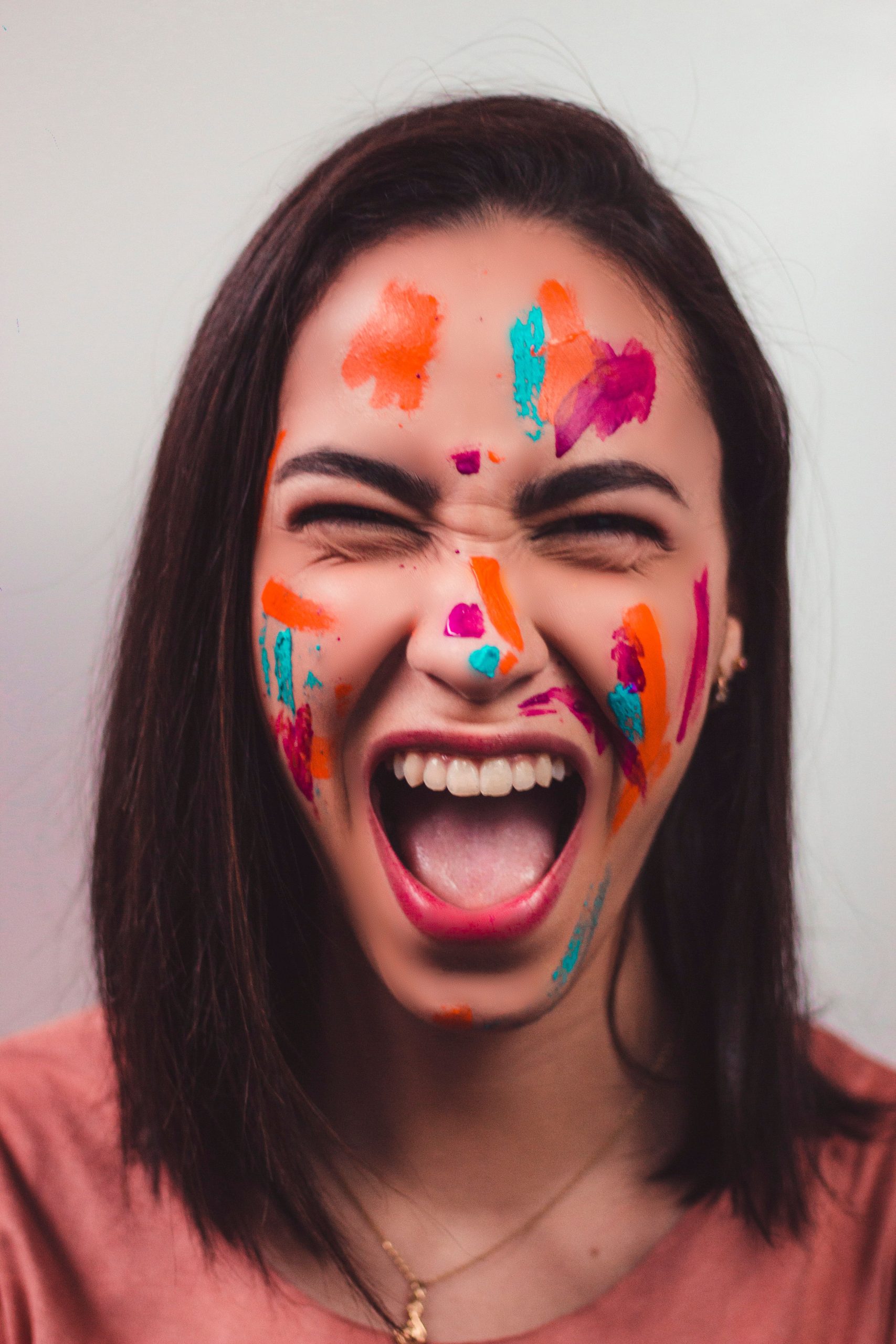 Accueil Portrait of a vibrant woman expressing joy with colorful face paint, isolated on a neutral background.